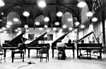Photograph of Glenn Gould playing one of four grand pianos that are lined up side by side